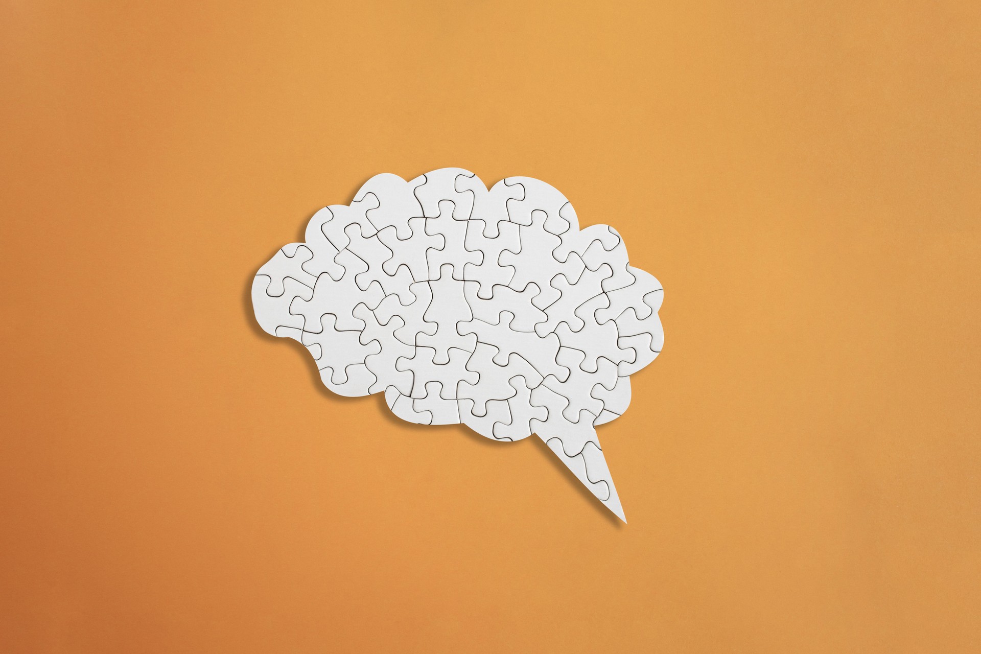 Brain shaped white jigsaw puzzle on orange background,  mental health and problems with memory concept